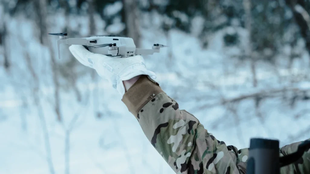 Un soldat en tenue de camouflage s'apprête à lancer un drone de reconnaissance en milieu forestier.
