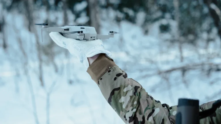Un soldat en tenue de camouflage s'apprête à lancer un drone de reconnaissance en milieu forestier.
