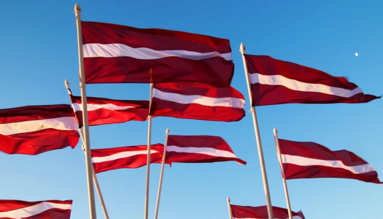 Plusieurs drapeaux de la Lettonie flottent au vent sous un ciel bleu clair et ensoleillé.