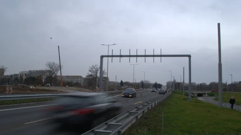 Automašīnas brauc pa šoseju zem pelēkām debesīm, raksturojot ikdienas satiksmi uz lielceļa.
