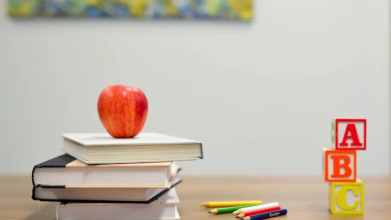 Sarkans ābols uz grāmatu kaudzes un krāsaini kluči, simbolizējot izglītības un pedagoģijas jomas vakances.