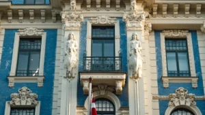 Latvijas karogs pie vēsturiskas ēkas fasādes, simbolizējot valsts nacionālo identitāti un nākotni.