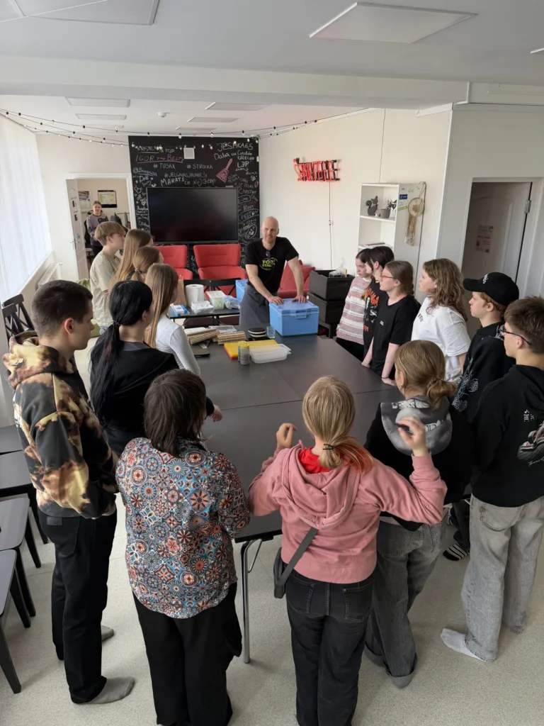 Un instructeur montre du matériel de cuisine à des jeunes debout autour d'une table noire.