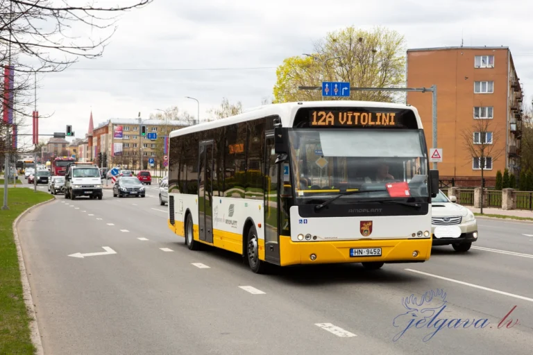 Un bus blanc et jaune Amoplant circulant sur une route urbaine avec l'affichage 12A VĪTOLIŅI.