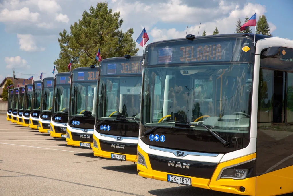 Rindā novietoti vairāki jauni dzelteni un balti MAN autobusi ar galamērķa norādi Jelgava.
