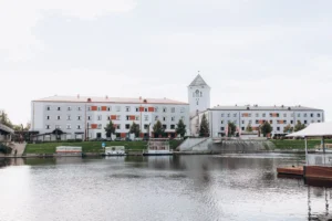 Skats uz Jelgavas Svētās Trīsvienības baznīcas torni un ēkām pie upes ar pietauvotām laivām.