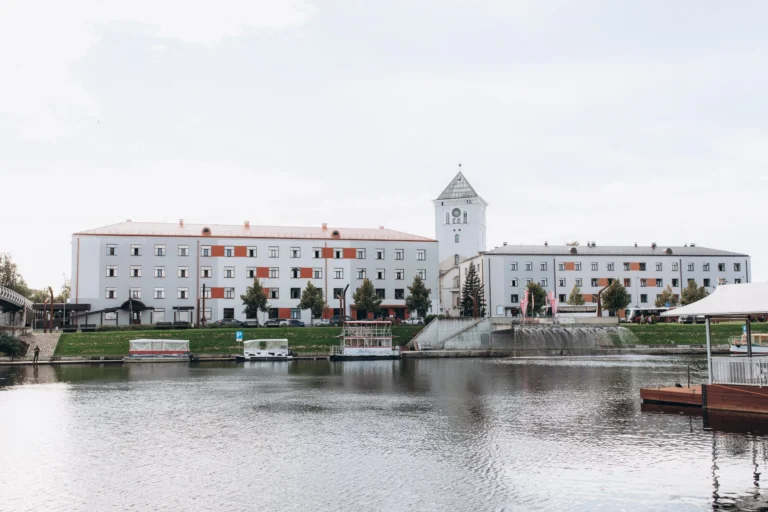 Skats uz Jelgavas Svētās Trīsvienības baznīcas torni un ēkām pie upes ar pietauvotām laivām.