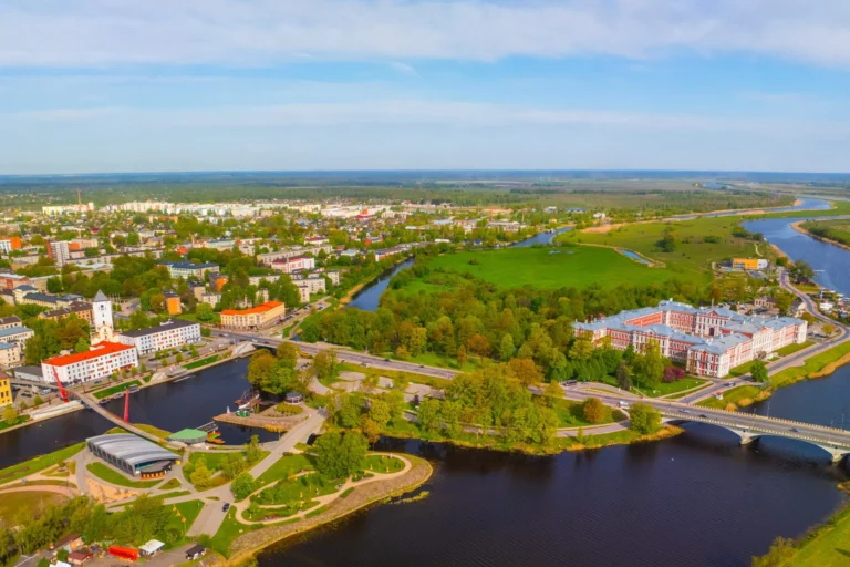 Aerofotoattēls ar Jelgavas pilsētu, pili, upēm un zaļiem parkiem zem skaidrām zilām debesīm.