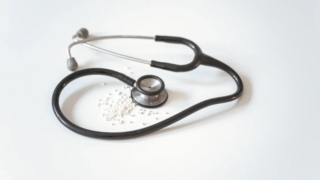 Melns un sudraba krāsas stetoskops uz balta fona, simbolizējot medicīnisko aprūpi un veselības pārbaudes.