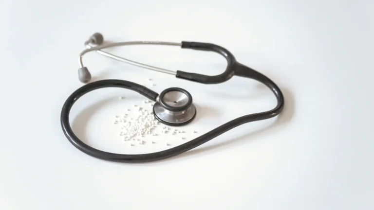 Melns un sudraba krāsas stetoskops uz balta fona, simbolizējot medicīnisko aprūpi un veselības pārbaudes.