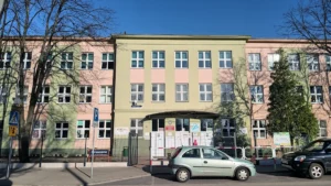 Skolas ēka ar gaišu fasādi un daudziem logiem, kas atgādina tipisku Latvijas izglītības iestādi.