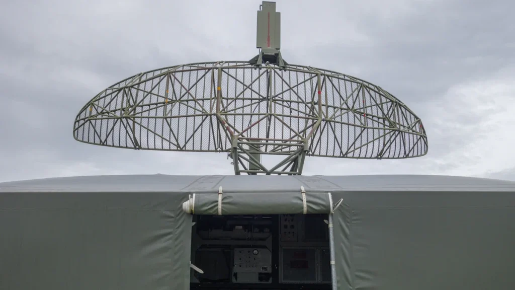 Militārs radars uz transportlīdzekļa bāzes pelēkās debesīs, kas simbolizē gaisa telpas uzraudzību.