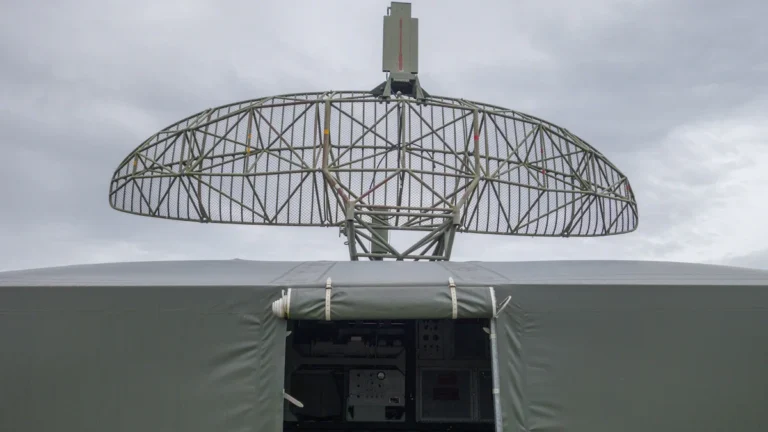 Militārs radars uz transportlīdzekļa bāzes pelēkās debesīs, kas simbolizē gaisa telpas uzraudzību.