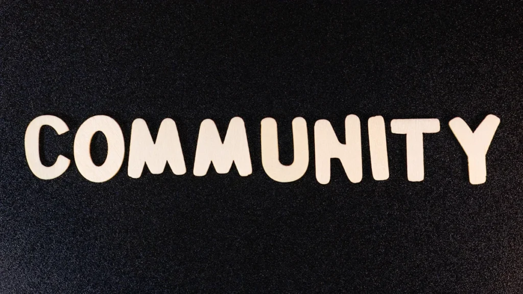 Uzraksts 'COMMUNITY' ar baltiem burtiem uz tumša fona, kas simbolizē kopienas un sadarbības nozīmi.