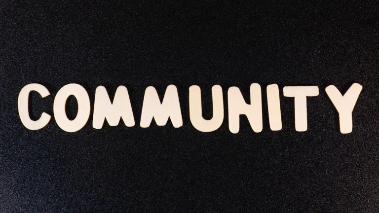 Uzraksts 'COMMUNITY' ar baltiem burtiem uz tumša fona, kas simbolizē kopienas un sadarbības nozīmi.