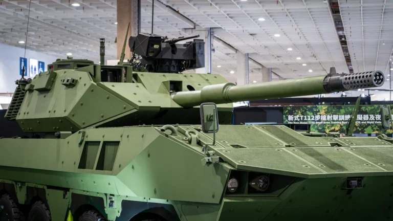 Mūsdienīgs bruņutransportieris ar lielgabalu aizsardzības izstādē, kas simbolizē fokusu uz jaunajām militārajām tehnoloģijām.