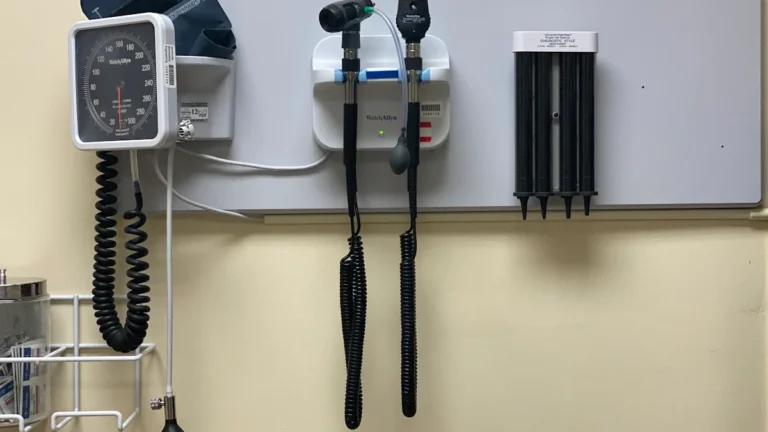 Pie sienas piestiprināts medicīniskais aprīkojums asinsspiediena mērīšanai un diagnostikai gaišā medicīnas kabinetā.