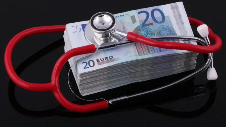 Medicīnas stetoskops novietots uz eiro banknošu kaudzes, uzsverot finanšu kontroli veselības aprūpes nozarē.