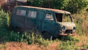 Vecs, sarūsējis zaļas krāsas mikroautobuss pamests pļavā, simbolizējot nolietotus transportlīdzekļus.