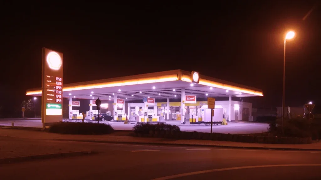 Izgaismota degvielas uzpildes stacija naktī, atspoguļojot tipisku pilsētas enerģētikas infrastruktūru.
