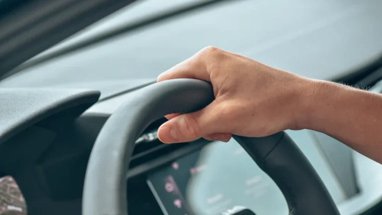 Autovadītāja roka uz automašīnas stūres, simbolizējot tiesības uz mobilitāti un dalību ceļu satiksmē.