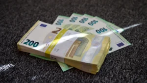 Eiro banknošu žūksnis ar 200 un 100 eiro zīmēm uz tumša paklāja fona.
