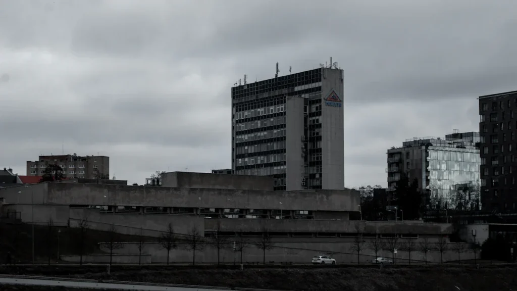 Mūsdienīga stiklota biroju augstceltne Viļņas biznesa rajonā uz mākoņainu debesu fona.