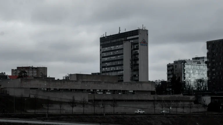 Mūsdienīga stiklota biroju augstceltne Viļņas biznesa rajonā uz mākoņainu debesu fona.