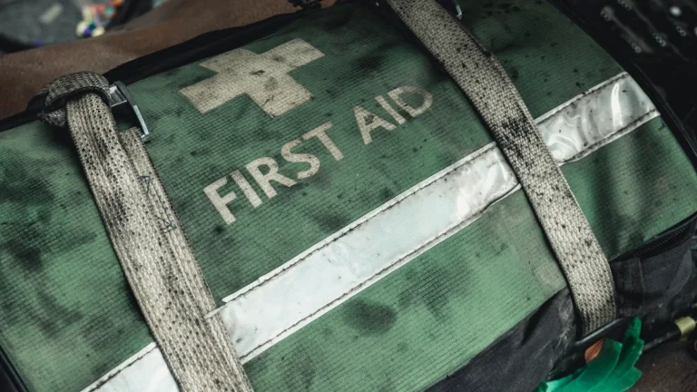 Zaļa pirmās palīdzības aprīkojuma soma ar labi saskatāmu uzrakstu "First Aid" un baltu medicīnas krustu.