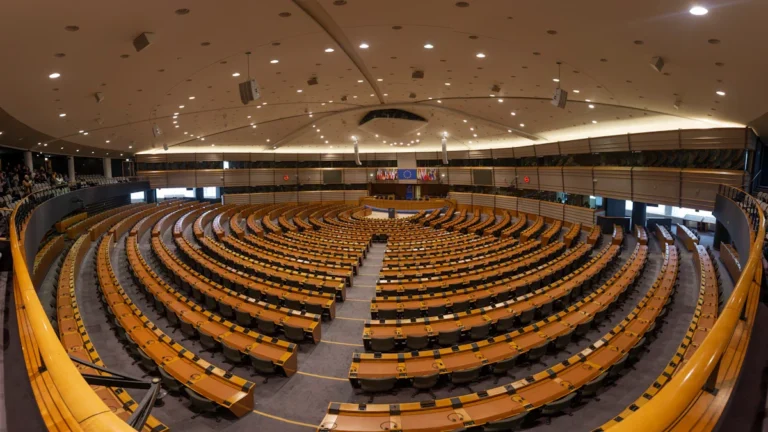Plaša parlamenta sēžu zāle ar pusloka formā izkārtotām sēdvietām un koka galdiem.