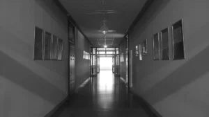 Tukšs skolas gaitenis melnbaltā krāsā, kas simbolizē gaidāmās pārmaiņas un neskaidrību izglītības nozarē.