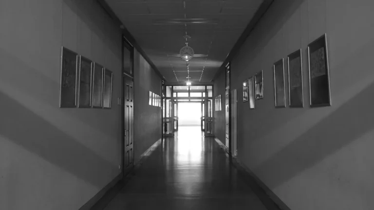 Tukšs skolas gaitenis melnbaltā krāsā, kas simbolizē gaidāmās pārmaiņas un neskaidrību izglītības nozarē.