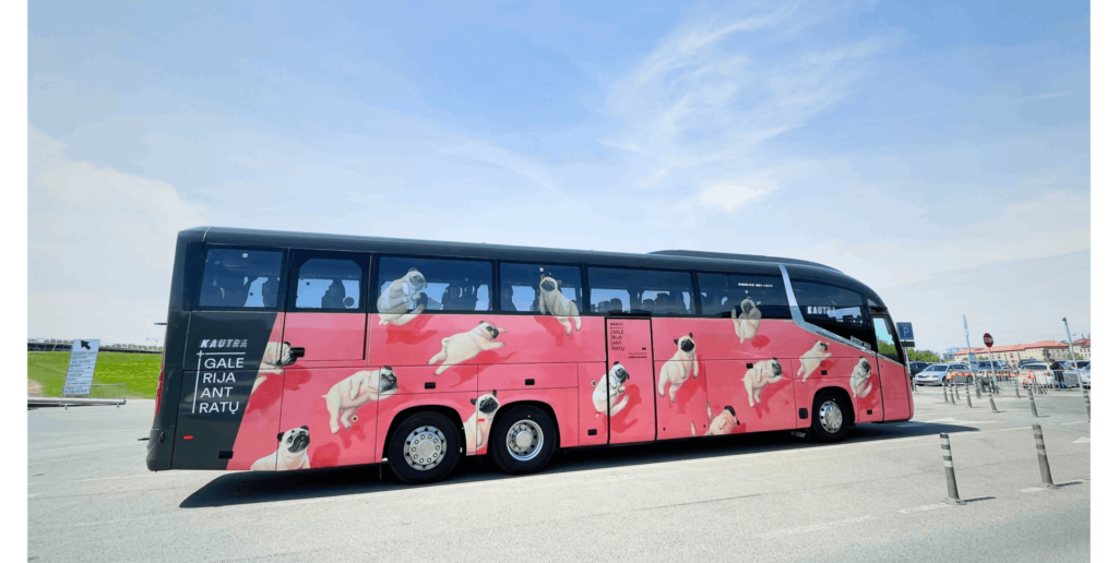 Melns autobuss ar rozā apakšdaļu, uz kuras attēloti daudzi mazi mopšu suņi dažādās pozās.