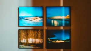 Četri ierāmēti mākslas darbi pie gaišas sienas, izgaismoti ar siltu gaismu modernā mākslas galerijā.