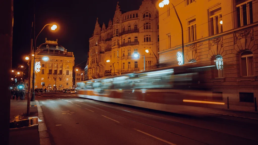 Izplūdis tramvajs naktī brauc pa pilsētas ielu, radot kustības un gaismas efektu.