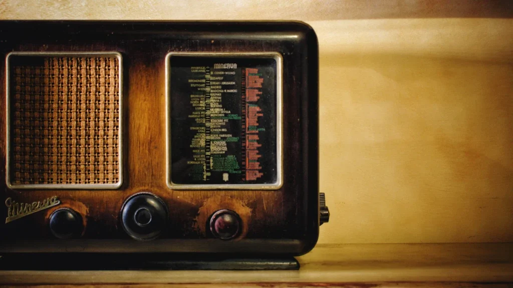 Senlaicīga tranzistoru radioaparāta tuvplāns ar fokusu uz frekvenču skalu tumšā, dramatiskā apgaismojumā.