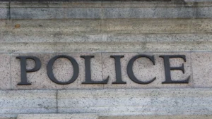 Tuvplāns ar tumšiem burtiem POLICE uz gaišas akmens sienas, norādot uz tiesībsargājošo iestāžu iesaisti.