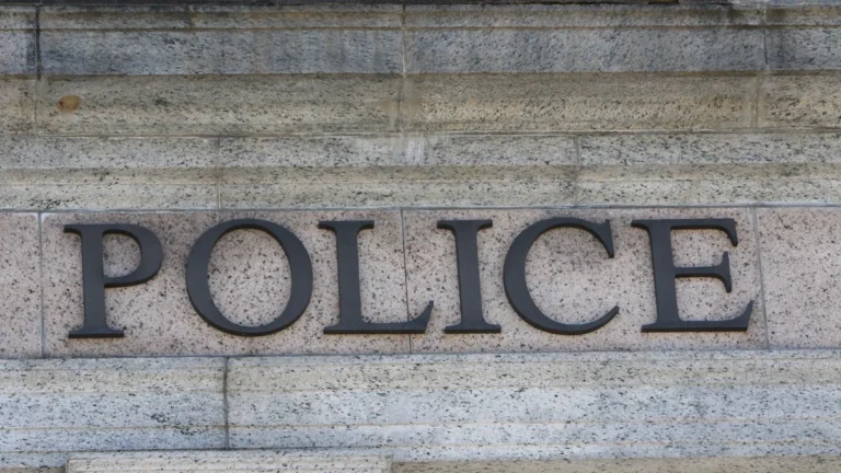 Tuvplāns ar tumšiem burtiem POLICE uz gaišas akmens sienas, norādot uz tiesībsargājošo iestāžu iesaisti.