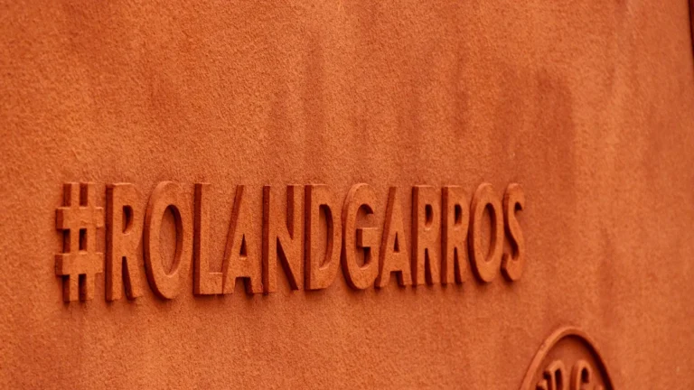 Sienā iekalts tēmturis Roland Garros uz oranža māla krāsas fona Parīzes tenisa stadionā.