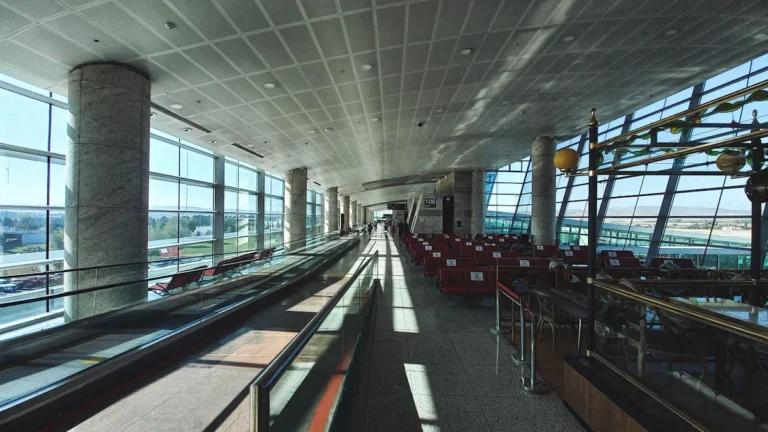 Moderna lidostas termināļa eja ar plašiem logiem, kas atspoguļo mūsdienīgu transporta mezglu arhitektūru.