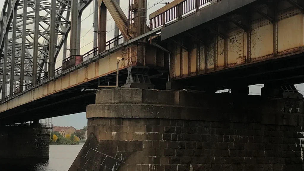 Dzelzceļa tilts Rīgā ar vilcienu, kas šķērso Daugavu, atspoguļojot pilsētas transporta infrastruktūras nozīmi.