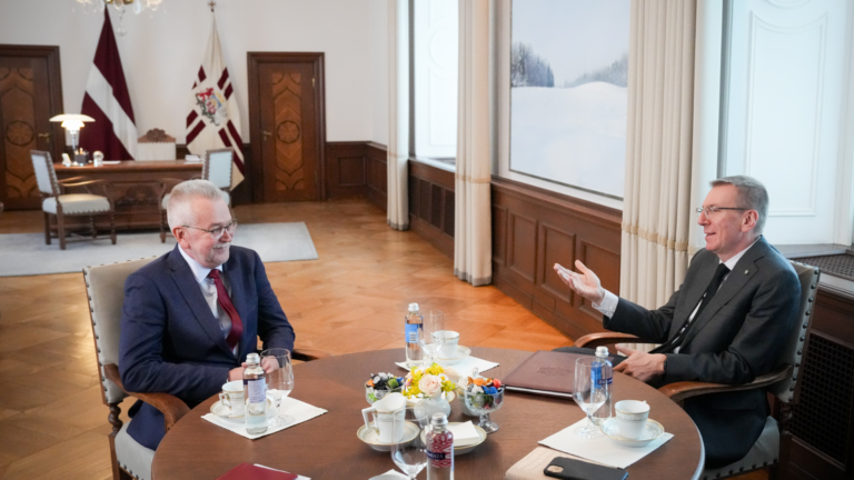 Divi kungi uzvalkos sēž pie apaļa galda un sarunājas telpā ar Latvijas valsts simboliku.