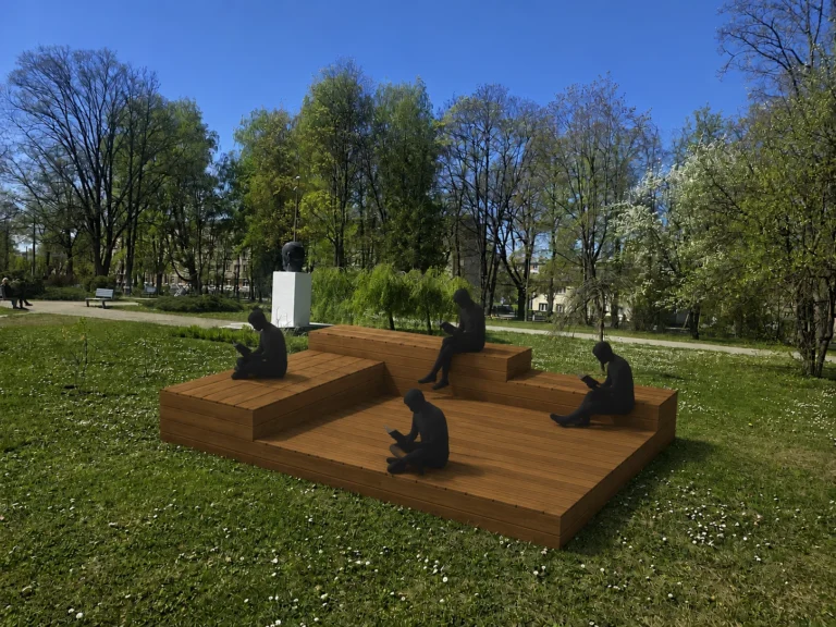 Četras tumšas silueta figūras sēž uz koka terases zaļā parkā un lasa grāmatas.