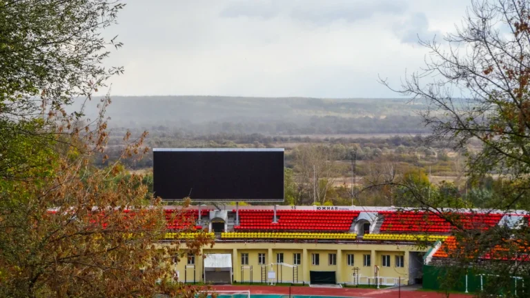 Futbola stadions ar sarkanām sēdvietām un lielu ekrānu vēsturiskā rezultāta paziņošanai.