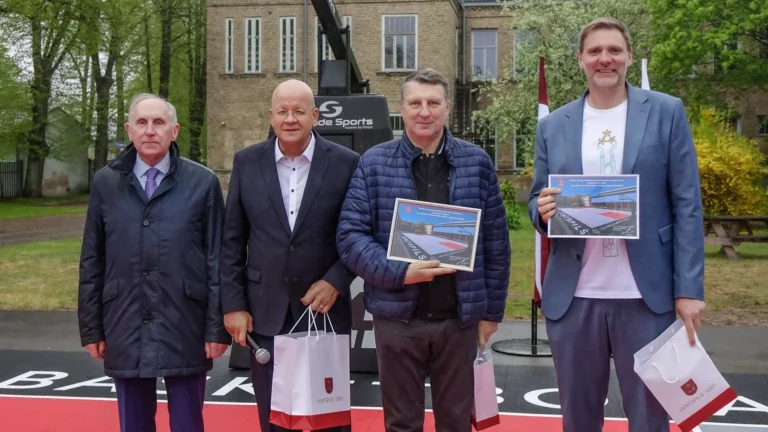Četri vīrieši uz basketbola laukuma fona tur rokās pateicības rakstus un Ventspils pilsētas dāvanu maisiņus.