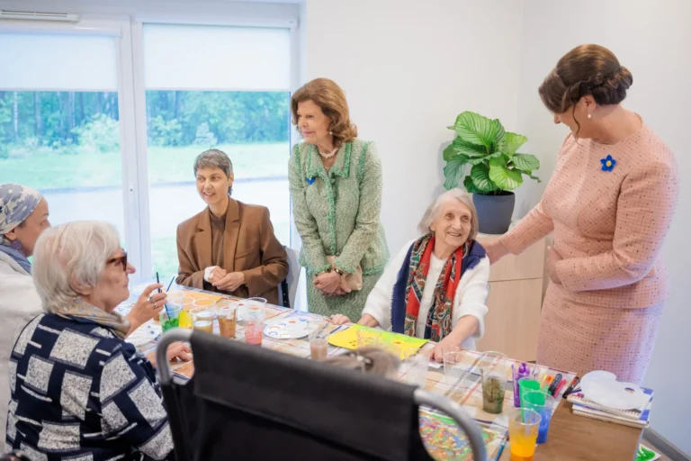 Karaliene Silvija un Andra Levite apmeklē seniorus, kuri pie galda nodarbojas ar radošu gleznošanu.