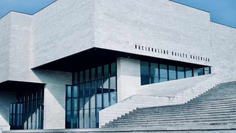 Mūsdienīga balta betona ēka Viļņā zem skaidrām zilām debesīm, simbolizējot pilsētas tehnoloģisko izaugsmi.
