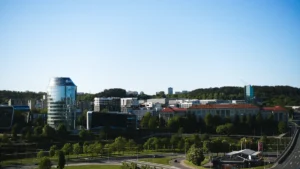 Mūsdienīgs skats uz Viļņas biznesa rajonu ar stikla debesskrāpjiem un zaļojošiem kokiem pilsētvidē.