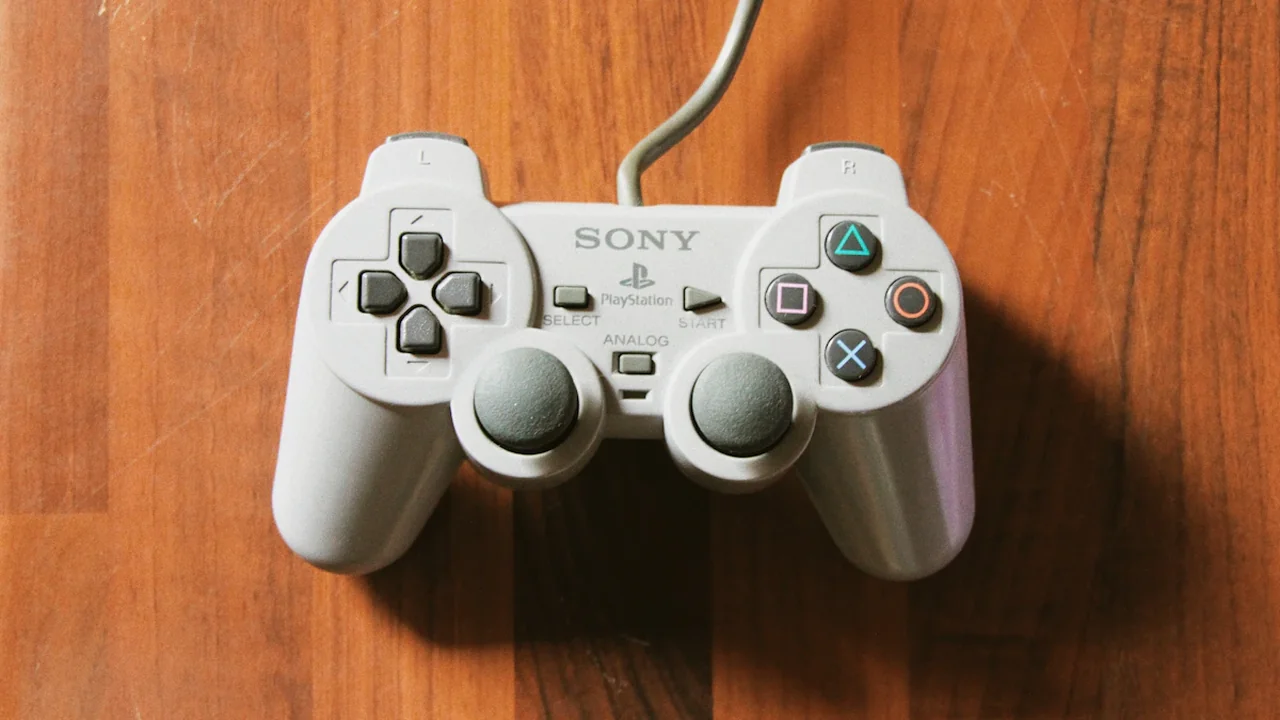 Pelēka Sony PlayStation spēļu pults uz koka virsmas Rīgā, Latvijā.