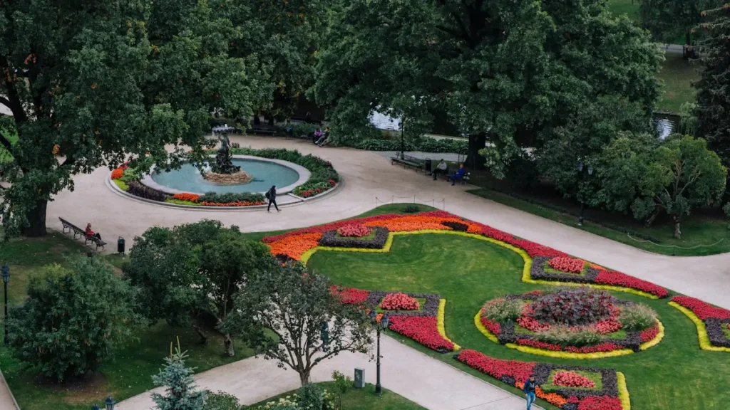 Vasaras diena Rīgas parkā ar strūklaku un krāšņiem ziedu stādījumiem pilsētas centrā.